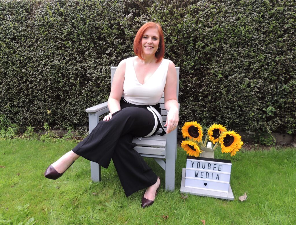 Rebecca sat on chair with Youbee Media sign 